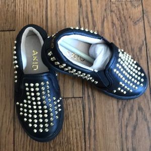 Akid black slip-on shoes with gold studs.